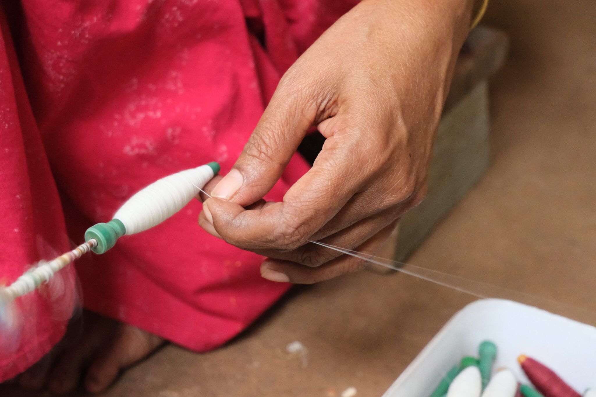 A weaver's hand guiding cotton thread onto a bobbin